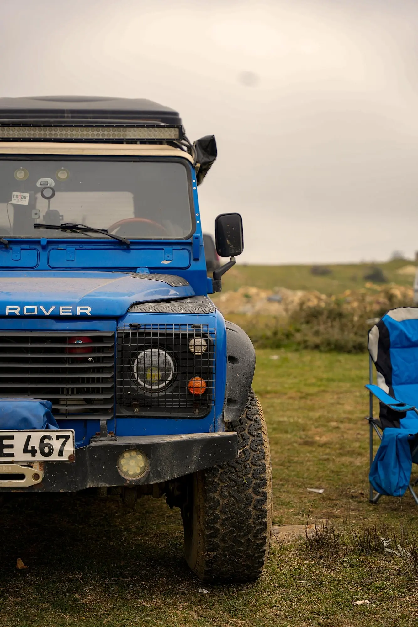 Klassischer Defender mit Campingstuhl auf der Wiese