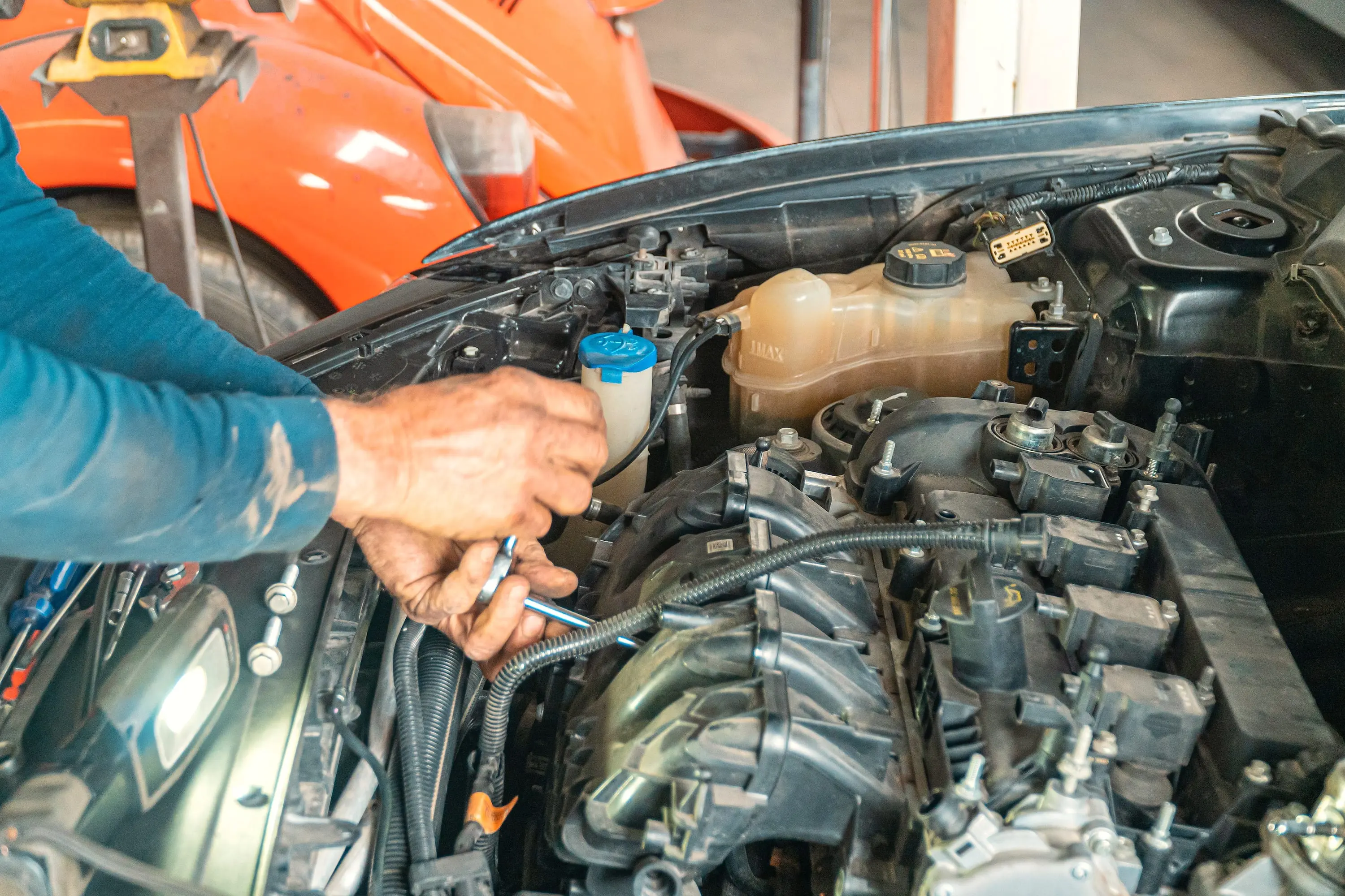 Ölige Hände mit Ringschlüssel am Motor, dahinter ein luftgekühlter Käfer